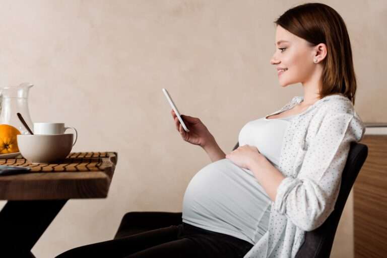 side view of happy pregnant woman using smartphone near tasty breakfast